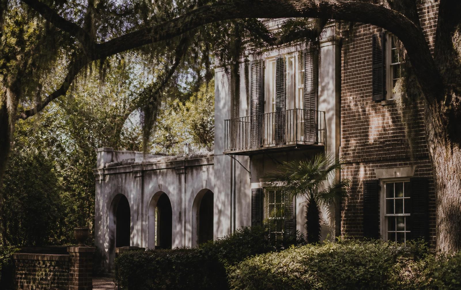 An older brick and stucco Northeast Florida home under live oaks in morning light.